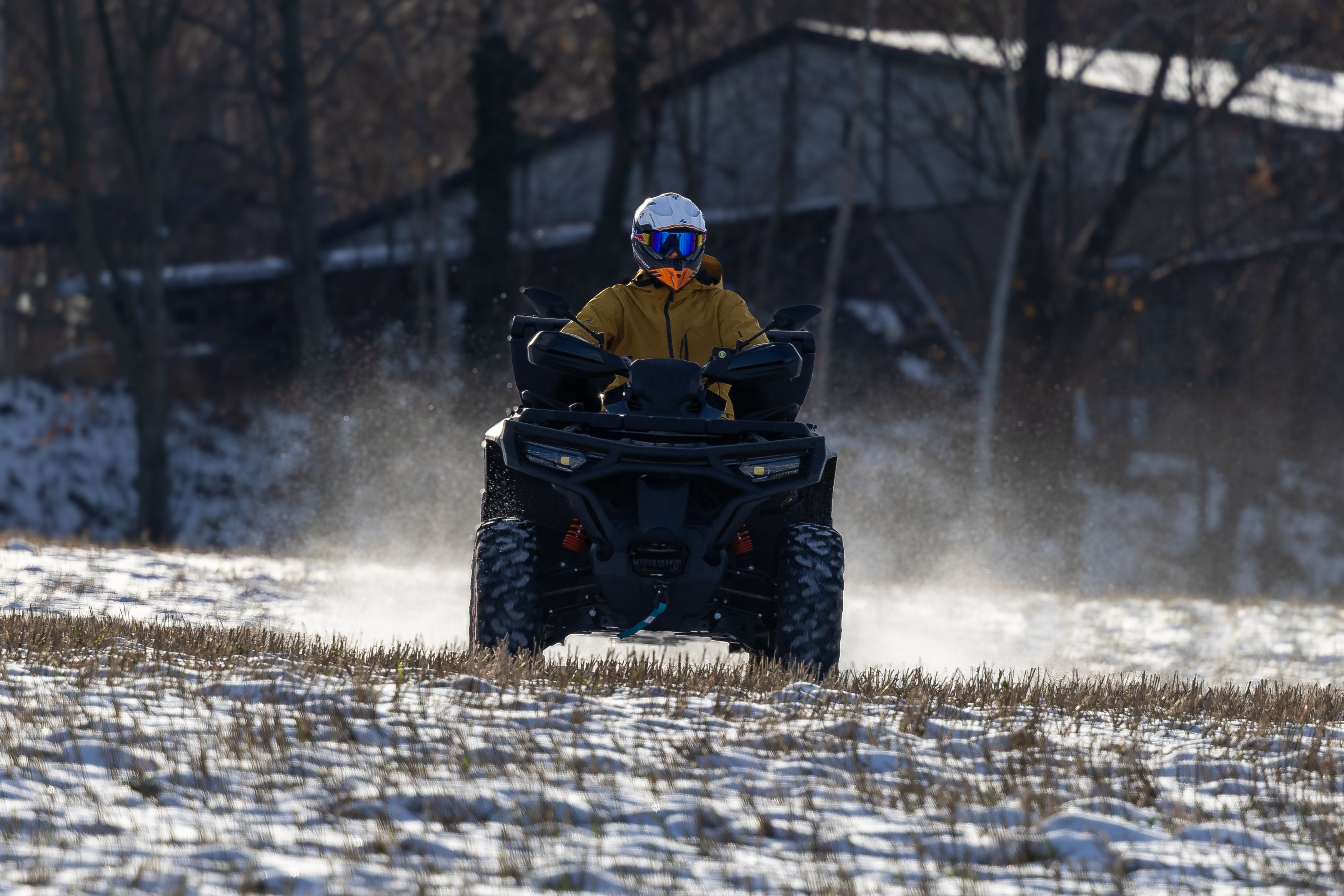A person on an ATV rides through a snow-covered field during winter, creating a dynamic scene.