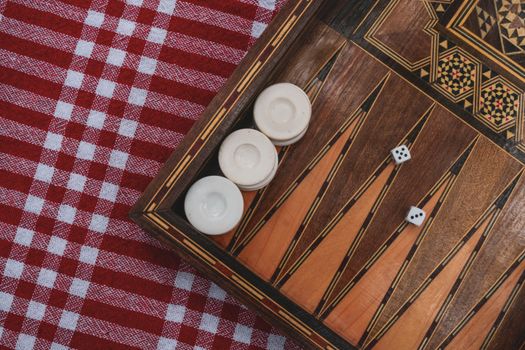 A close-up of a traditional backgammon set on a red checkered picnic blanket, showing dice and pieces.