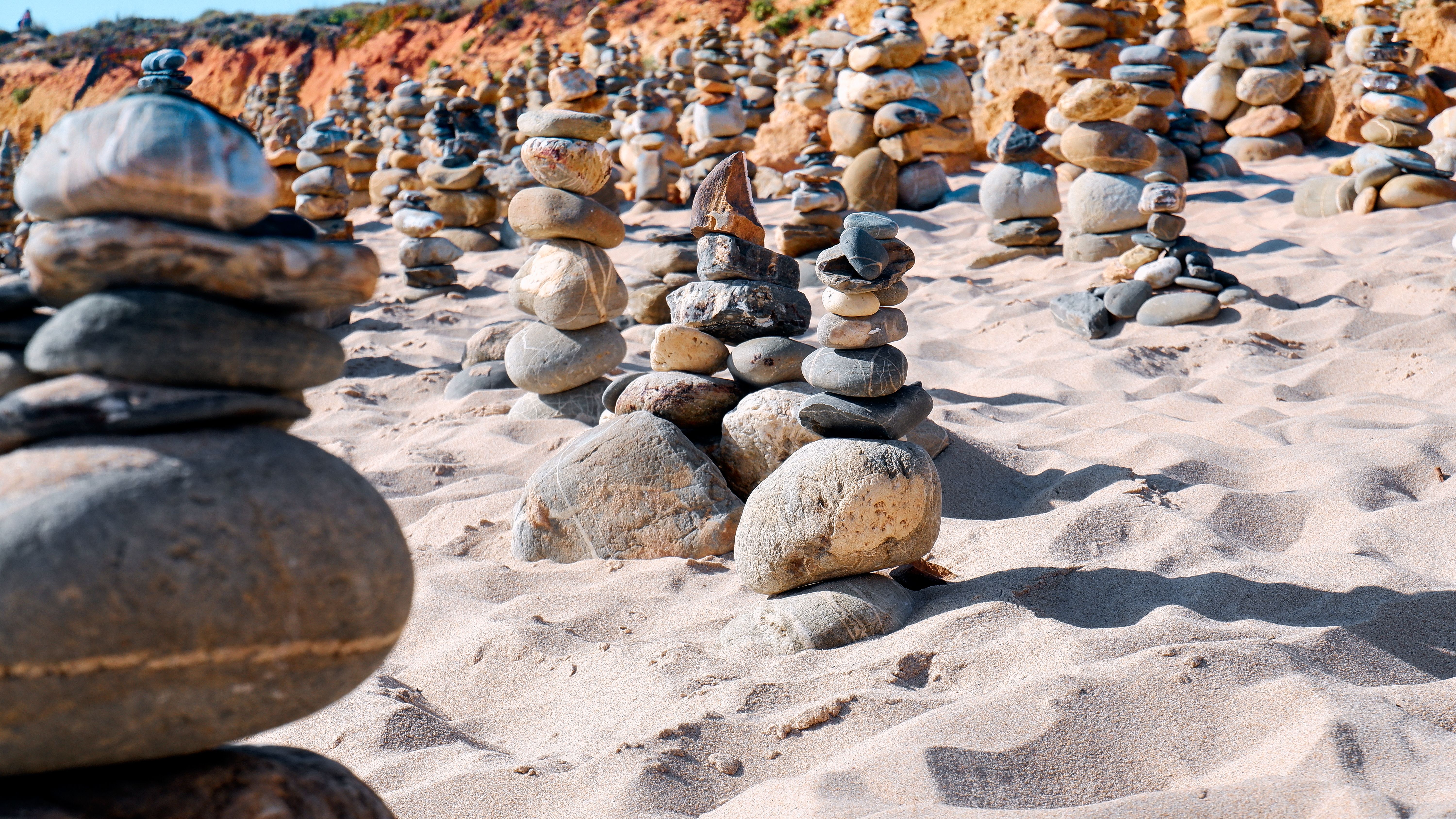 Balanced stone towers on a sandy beach in Vila Nova de Milfontes, Portugal, under a sunny sky.