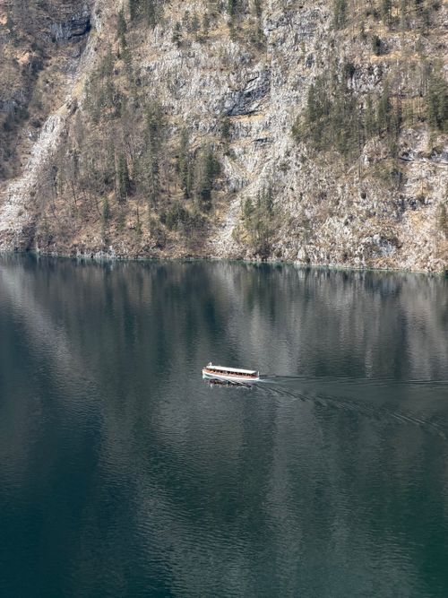 Free A peaceful boat floats on the tranquil waters of Königssee surrounded by towering cliffs and forests. Stock Photo