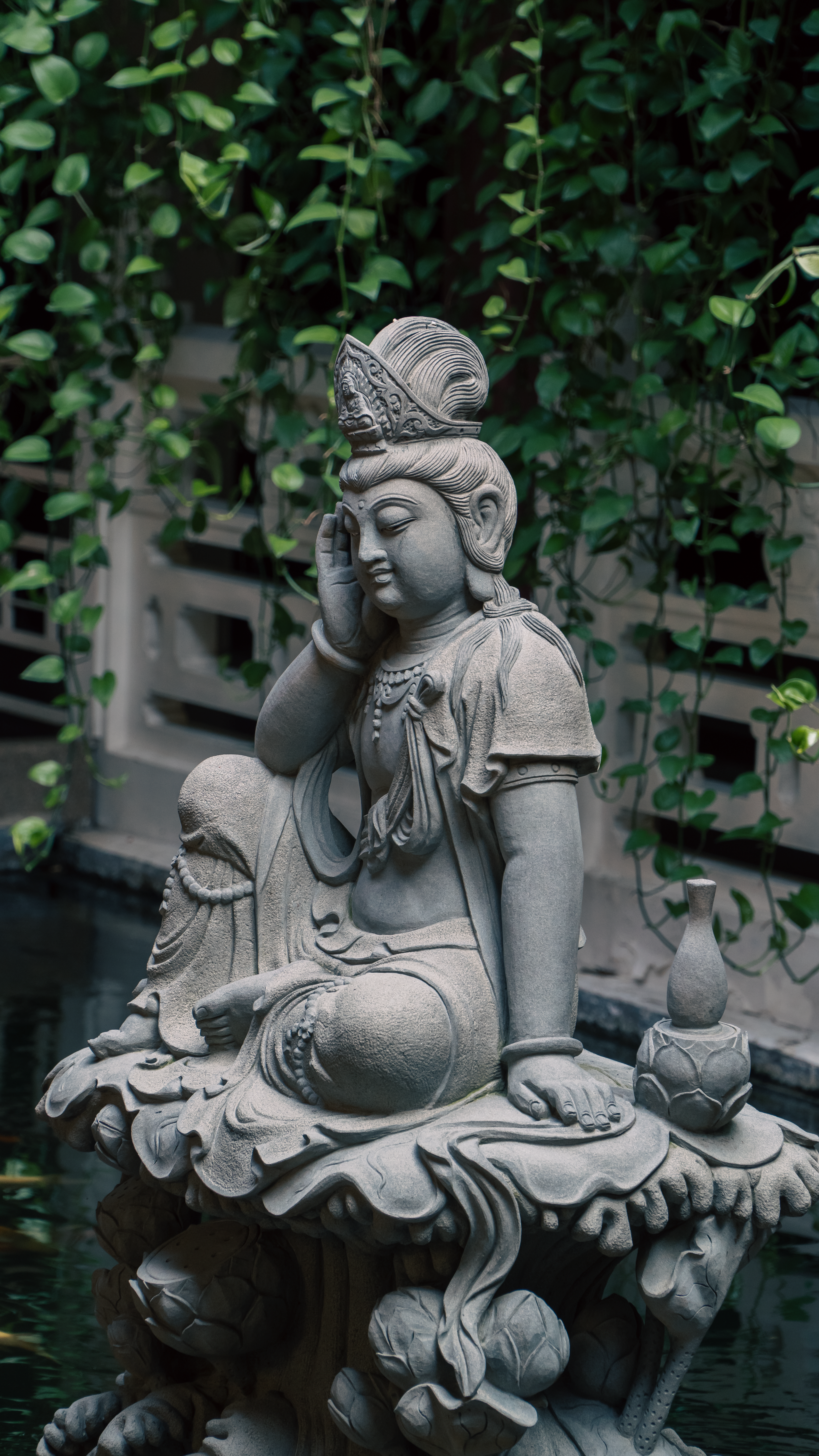 Peaceful stone Buddha statue surrounded by lush greenery in an outdoor garden.