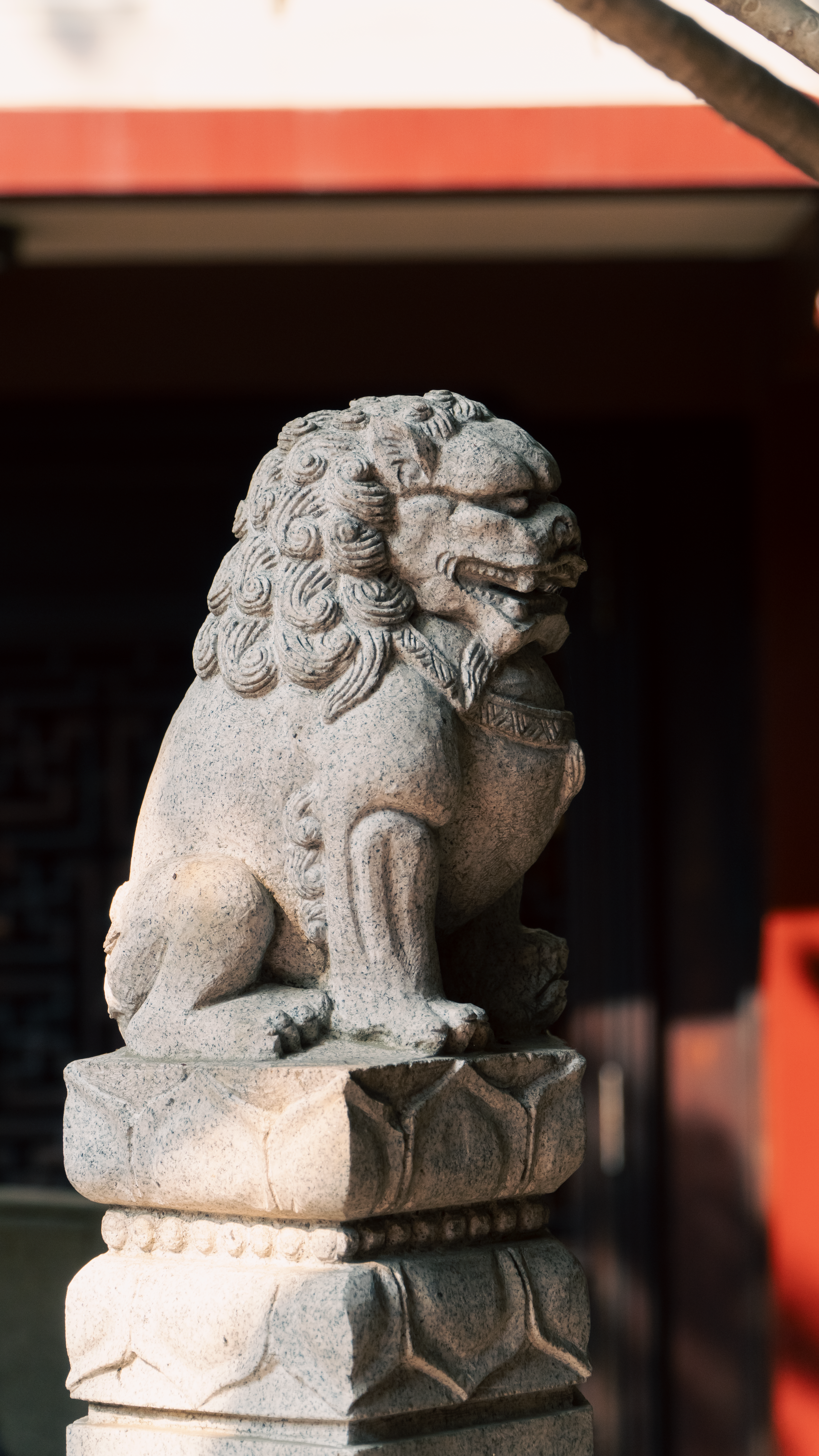 A carved stone lion statue outdoors, symbolizing protection and strength, with traditional Chinese architecture in background.