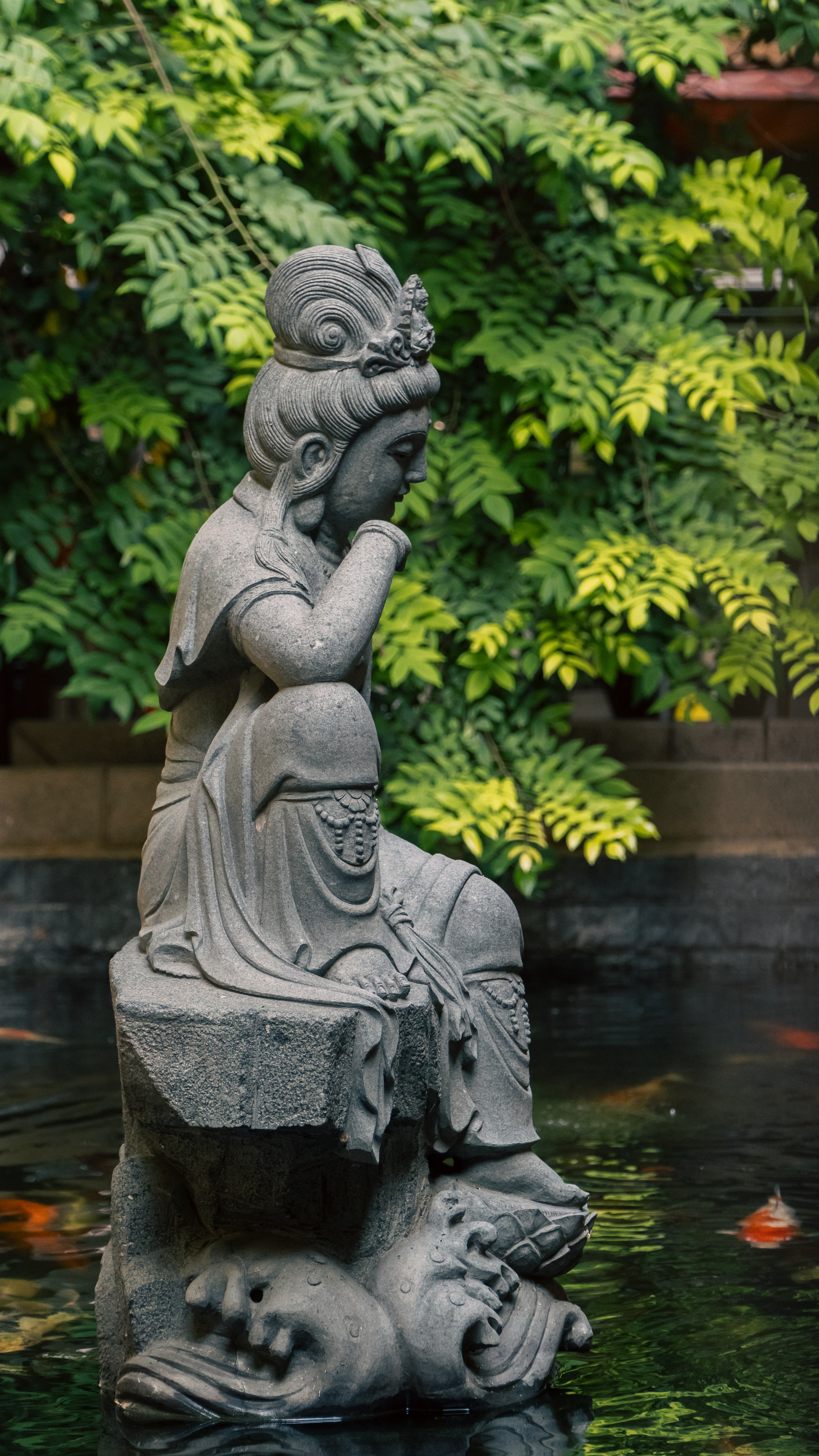 Elegant stone statue of a woman in a peaceful garden pond surrounded by lush greenery.