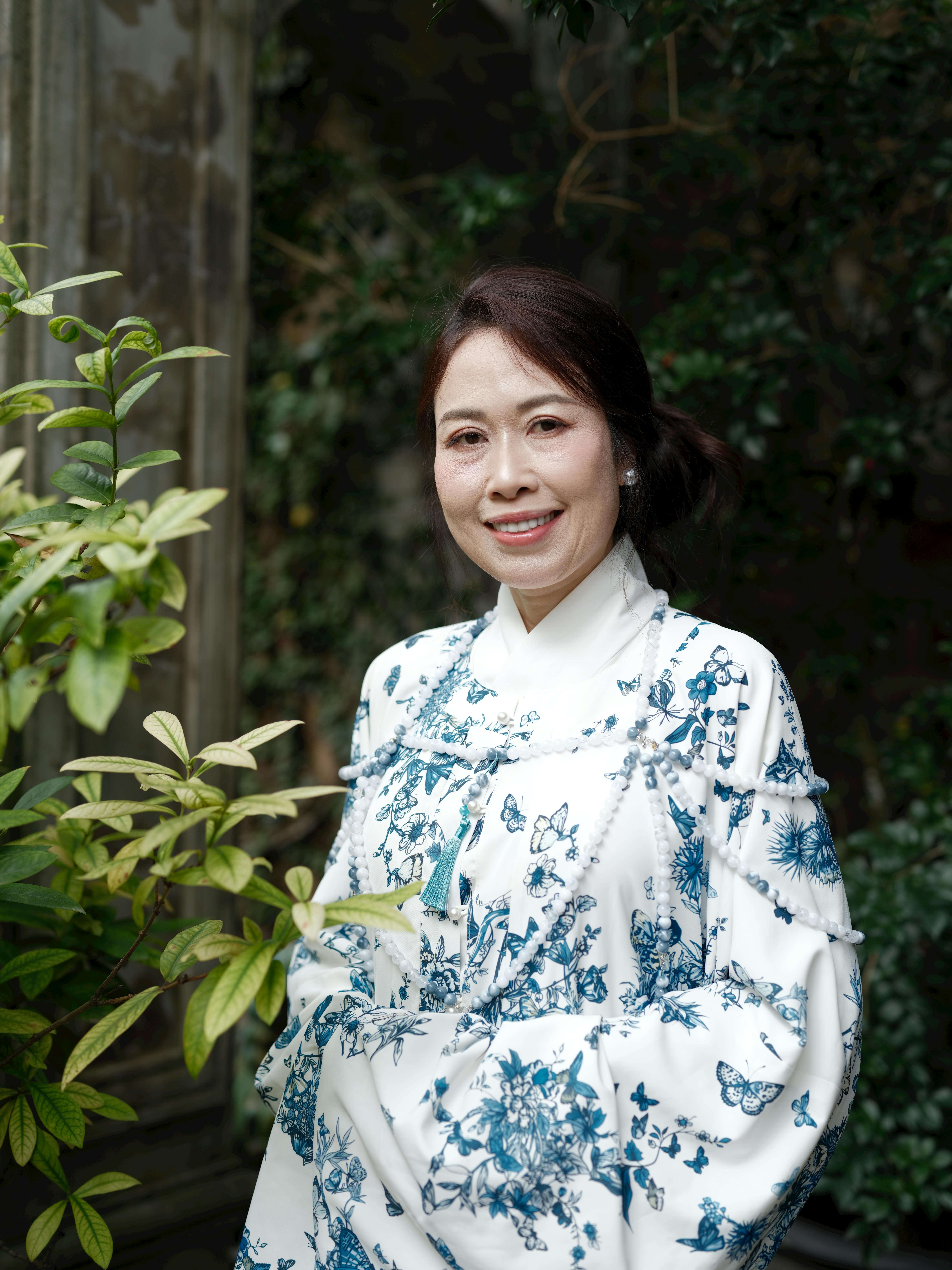 Elegant woman in hanbok surrounded by greenery, showcasing traditional fashion in a serene outdoor setting.