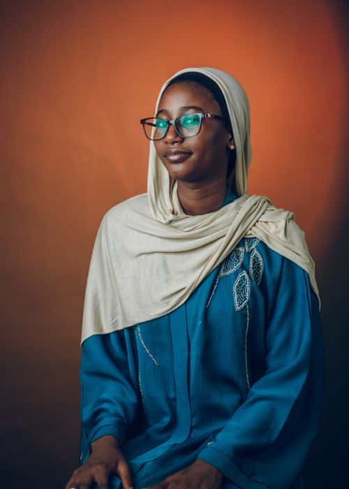Free Portrait of an African woman in traditional Hausa attire with a serene pose against an earthy background. Stock Photo