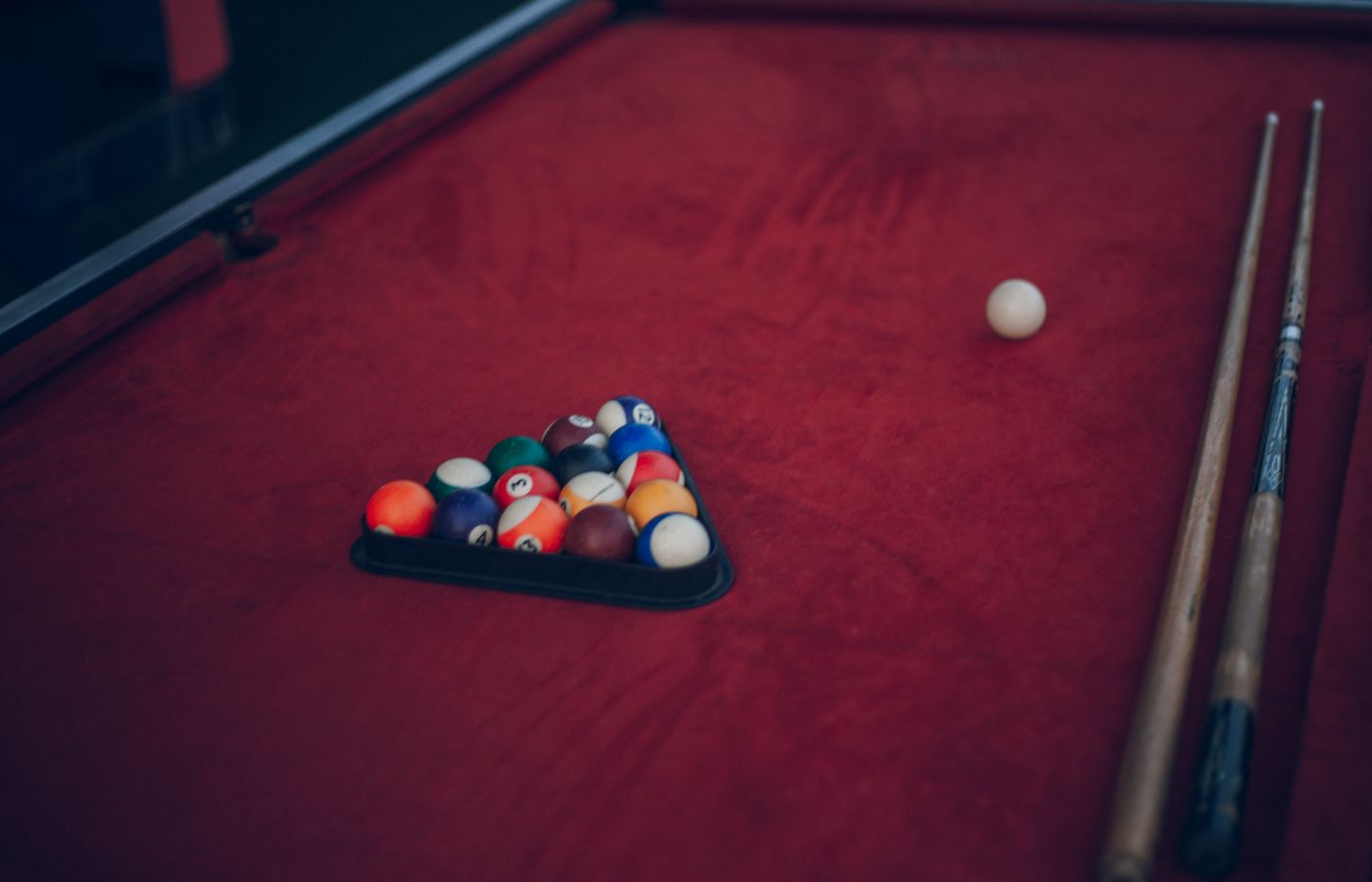 A classic billiard setup with a triangle of pool balls and cues on a red table.