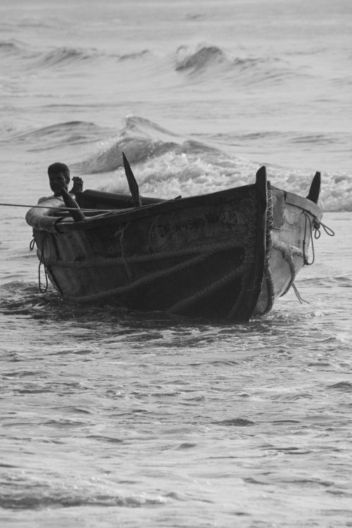 Free Black and white photo of a man rowing a wooden boat through ocean waves, capturing a serene maritime scene. Stock Photo