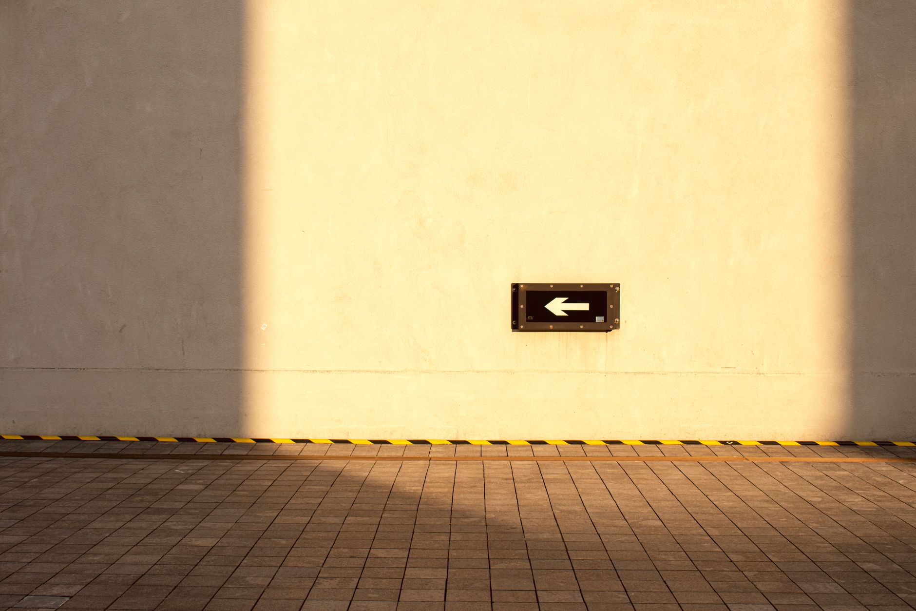 A minimalist arrow sign on a sunlit wall with tiled floor, creating a warm artistic composition.