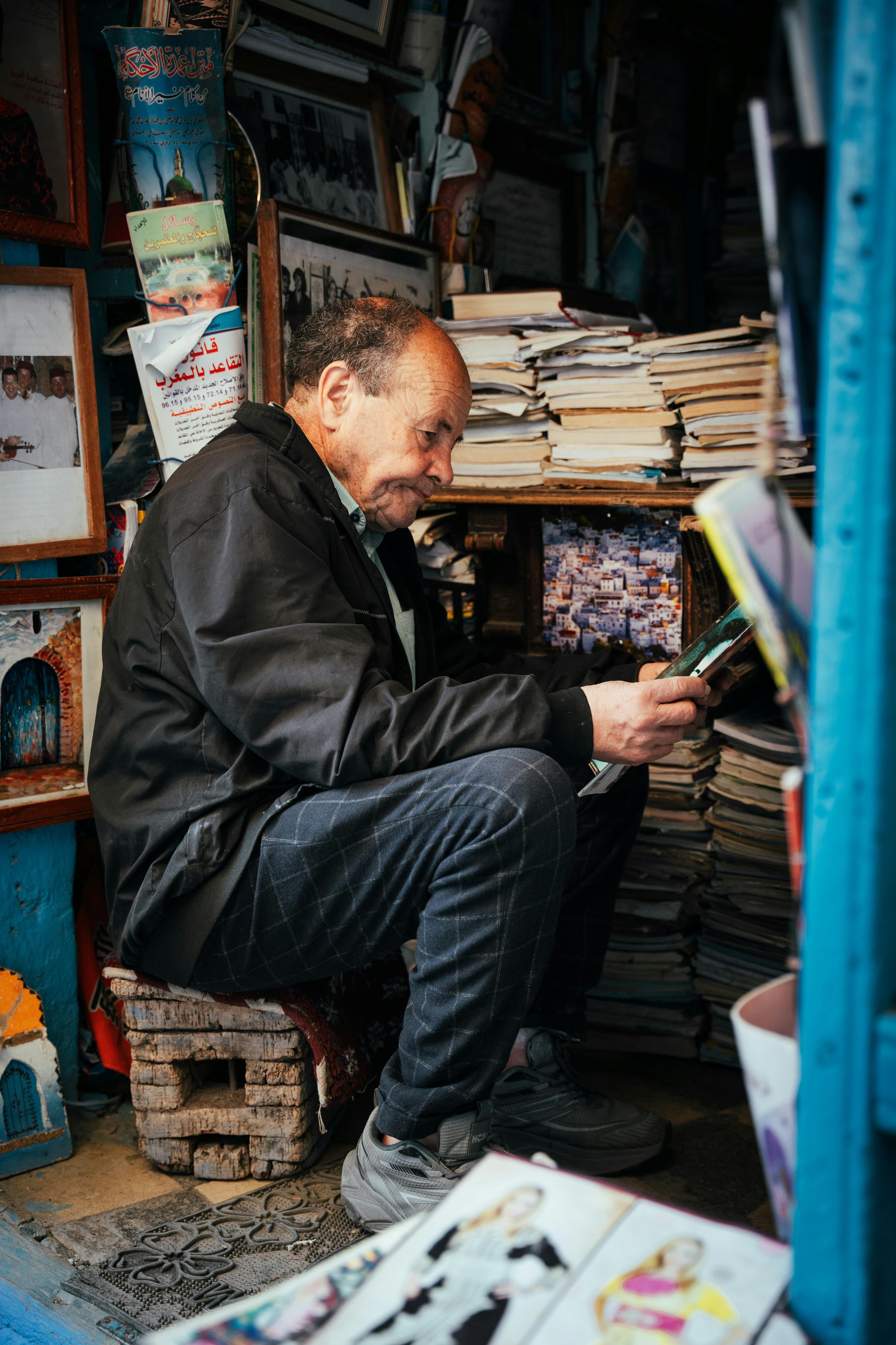 Senior man reading in a cozy Moroccan bookstore surrounded by stacks of books and photos.