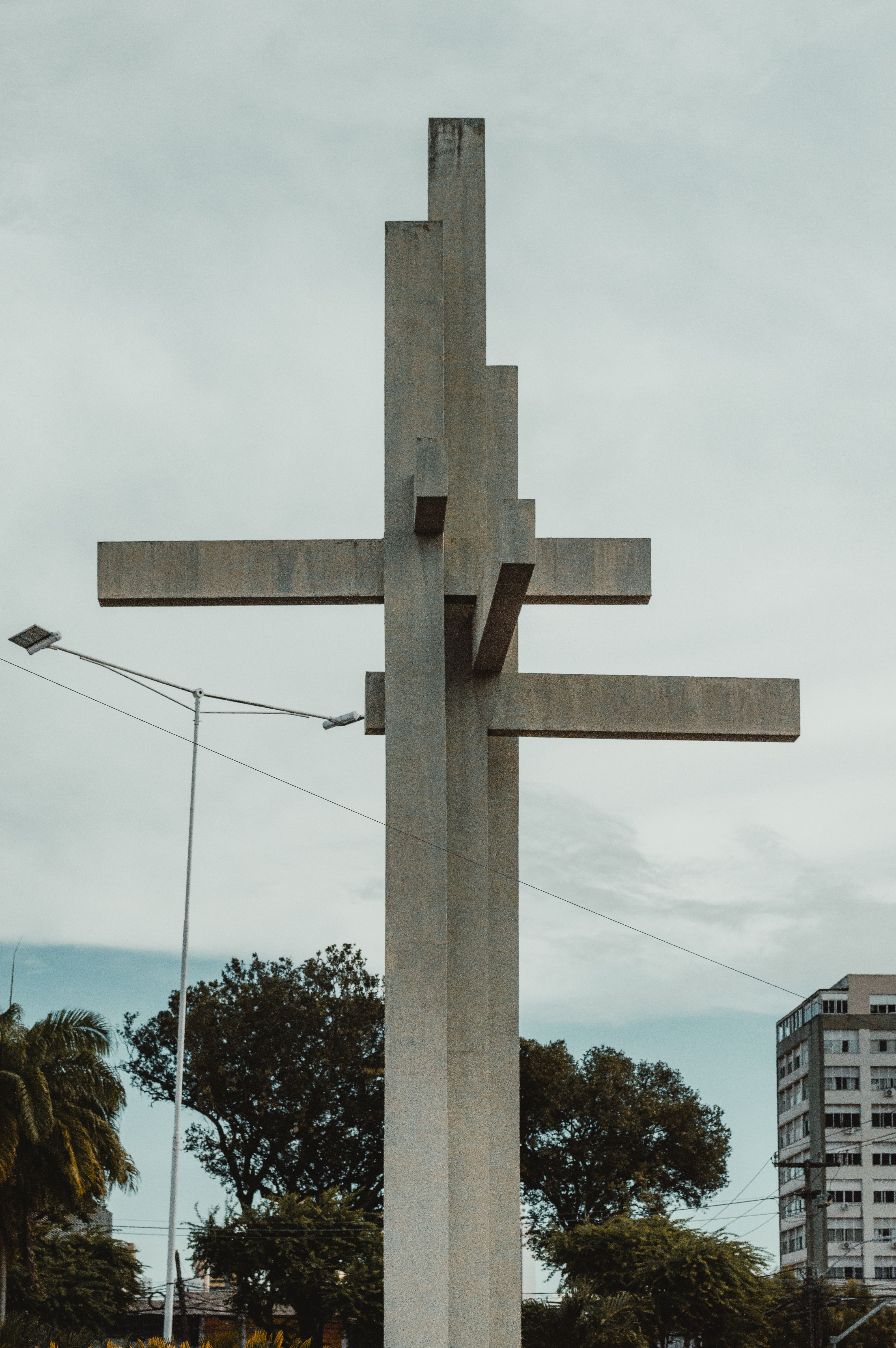 A towering modern cross sculpture contrasts against the urban backdrop of Natal, Brazil.