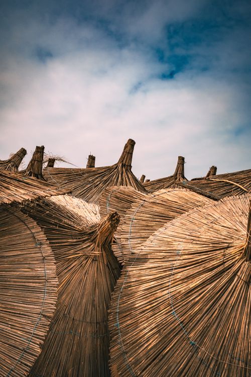 Free Rustic straw beach umbrellas under a cloudy sky at Golem Beach, Albania. Perfect for travel themes. Stock Photo