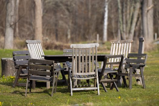 A group of rustic wooden chairs surrounds a table in an outdoor Swedish setting, exuding a peaceful vibe.