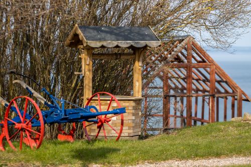 Free Scenic view of a wooden well and antique plow in Gränna, Sweden, with a lake view. Stock Photo