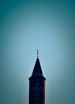 A solitary historic minaret silhouetted against a clear blue sky, capturing architectural elegance.