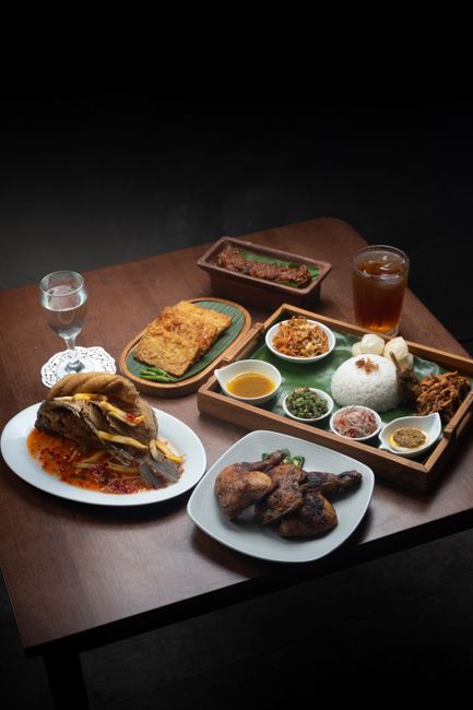 A variety of traditional Indonesian dishes displayed on a wooden table with dim lighting.