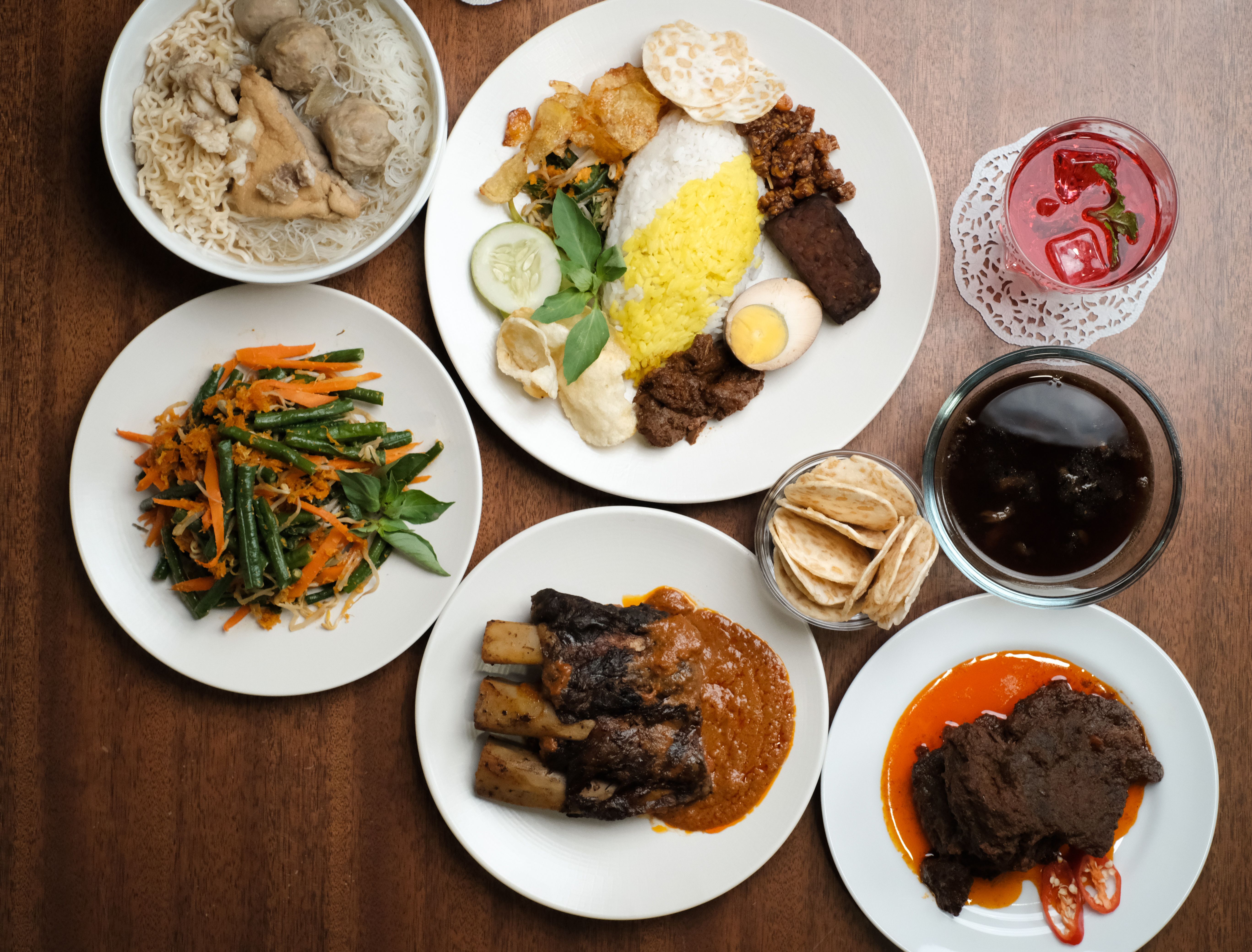A top-down view of a variety of traditional Indonesian dishes on a wooden table.