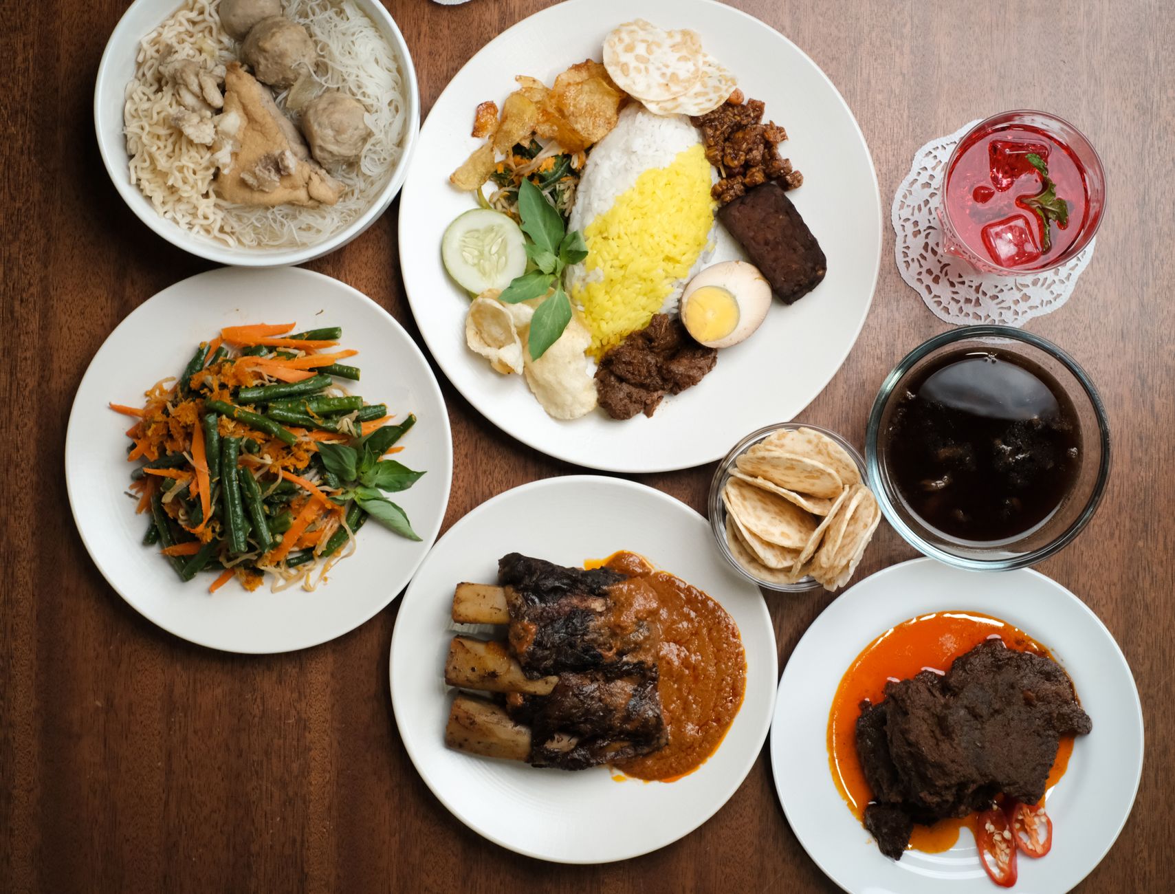 A top-down view of a variety of traditional Indonesian dishes on a wooden table.