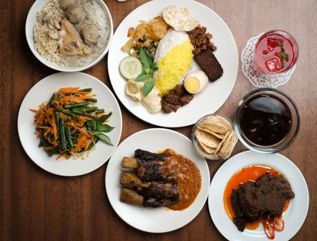 A top-down view of a variety of traditional Indonesian dishes on a wooden table.