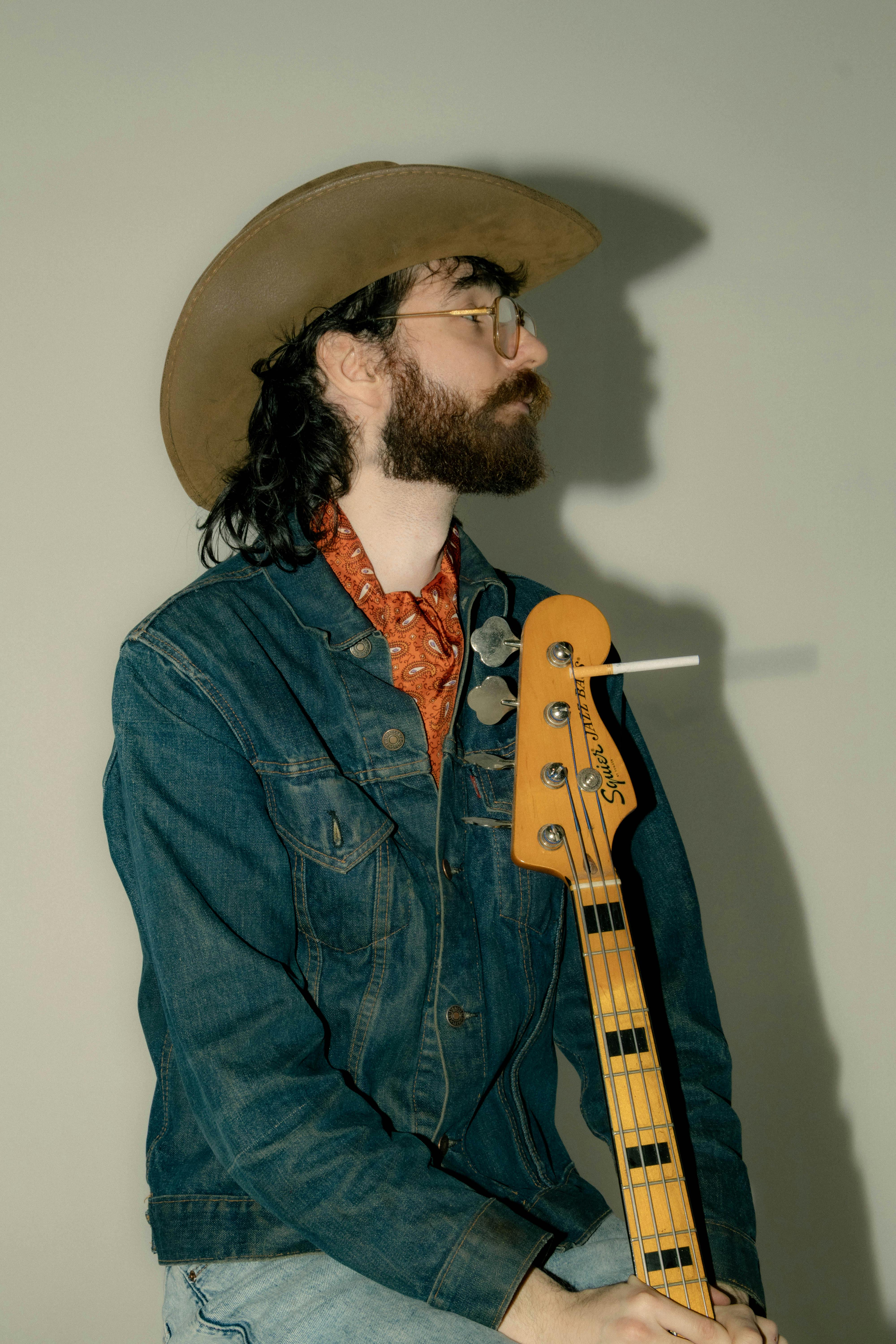 Portrait of a stylish musician wearing a cowboy hat and denim, holding a bass guitar.