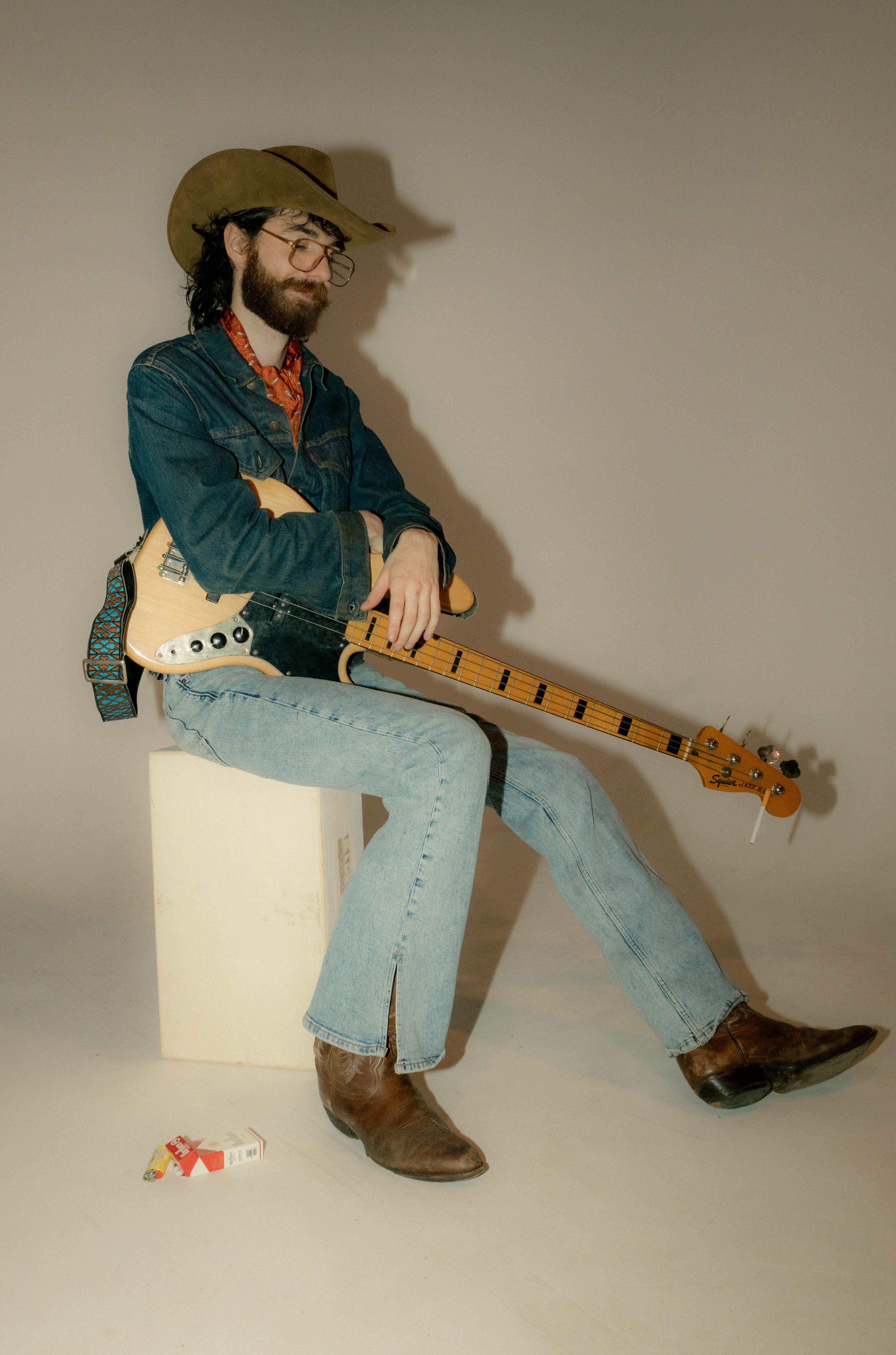 Musician in denim and cowboy hat with guitar, seated for a vintage-style portrait.