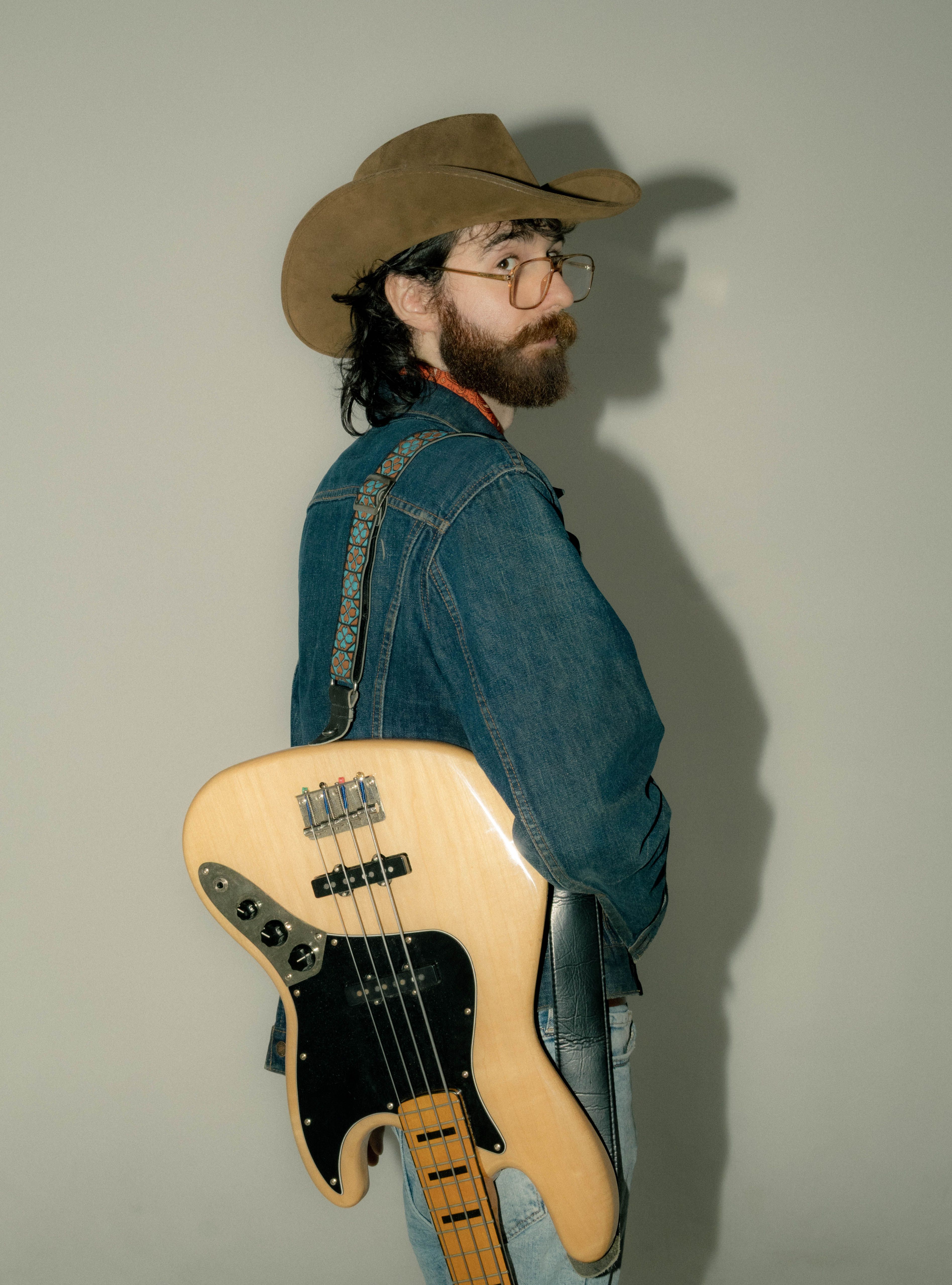 A stylish cowboy in a denim jacket holding a bass guitar, exuding a vintage Western vibe.