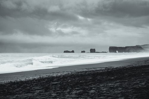 Free Moody black and white image of Iceland's black sand beach with dramatic waves under stormy skies. Stock Photo