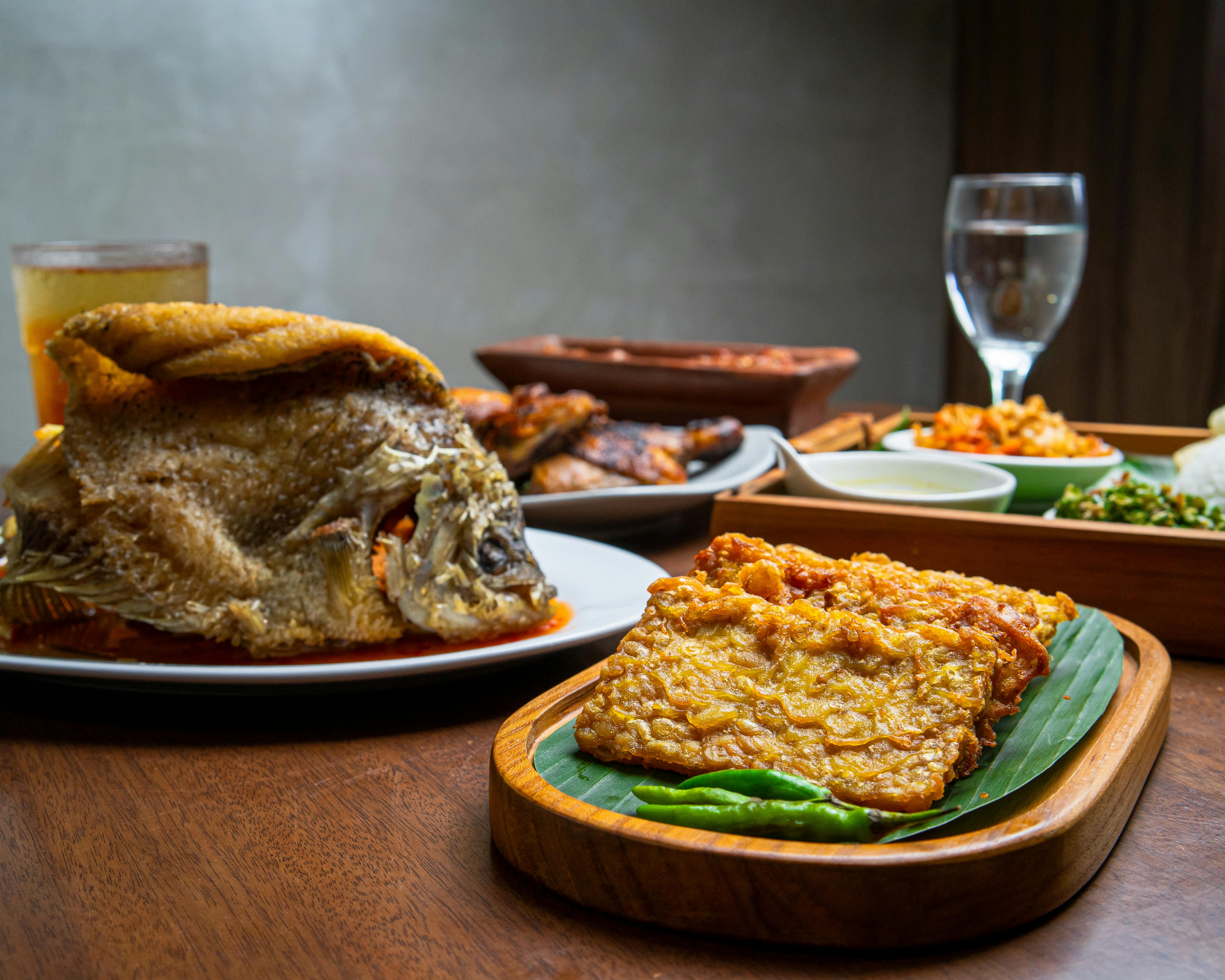 Delicious Indonesian traditional dishes including fried fish and tempeh on a wooden table.