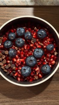 A vibrant fruit bowl featuring blueberries, pomegranate seeds, and chocolate chips on a wooden table.