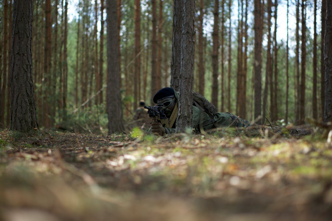 Мужчина в военной форме и рюкзаке лежит на земле в окружении деревьев