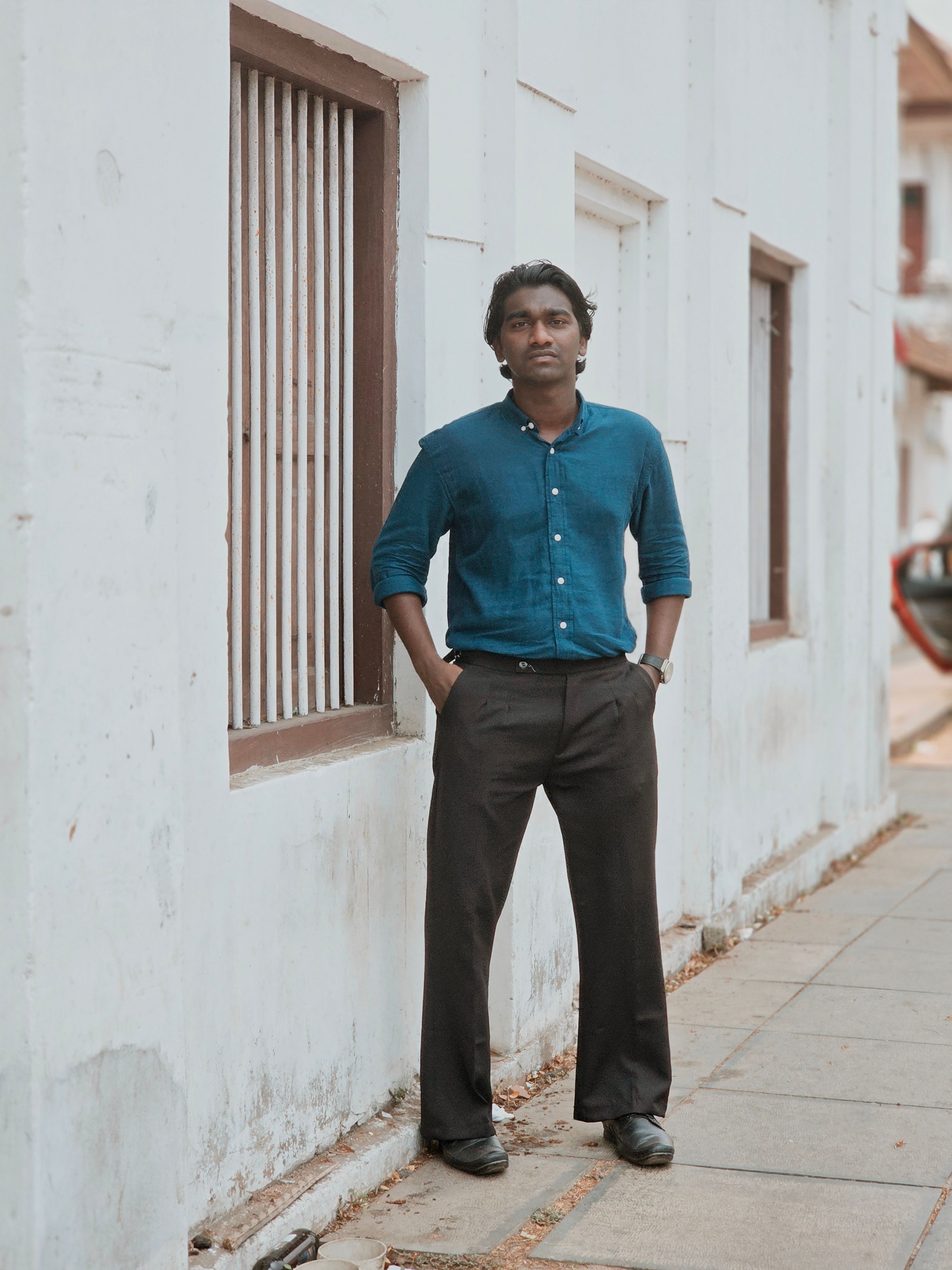 Man in blue shirt standing confidently next to an urban building, exuding a relaxed yet professional demeanor.