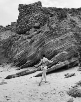 Black and white photo of a woman in a swimsuit on a scenic rocky beach.