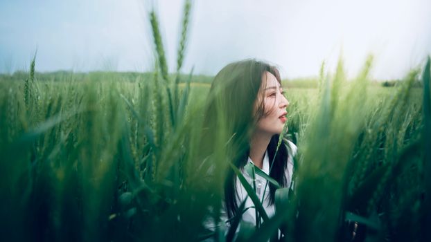 A serene portrait of a woman amidst a vibrant green wheat field under a clear sky.