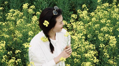 Free A woman in a white top enjoys a sunny day surrounded by vibrant yellow mustard flowers. Stock Photo