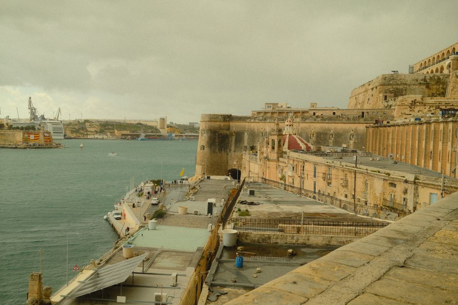 Scenic view of Malta's fortifications along the waterfront with a cruise ship in the port.