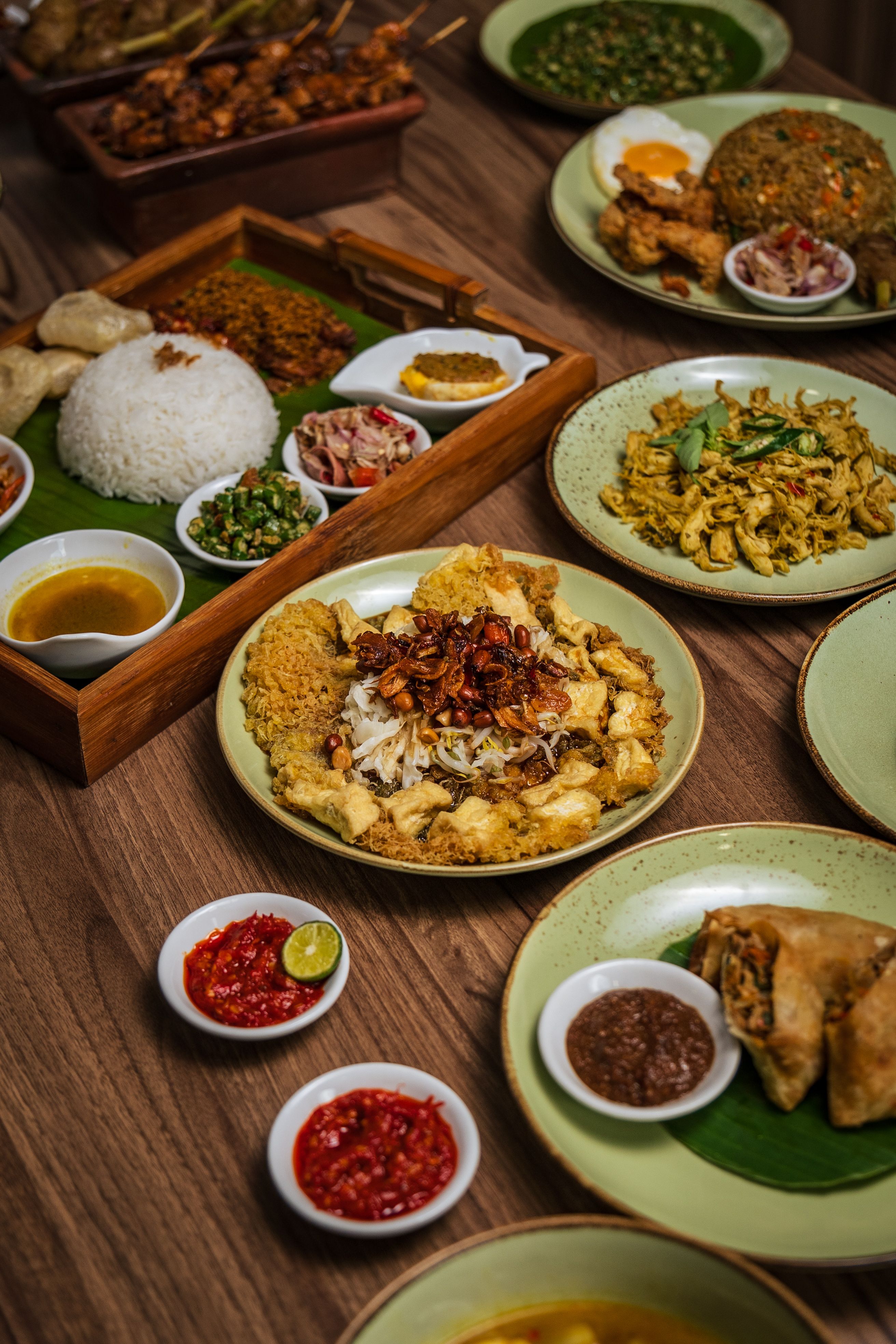 Table en bois foncé garnie de plats indonésiens : riz blanc, tofu frit, sambals et poulet effiloché
