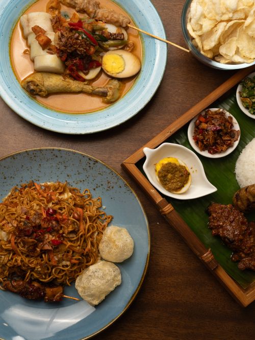 Free Top view of various Indonesian dishes, including Nasi Padang, noodles, and snacks on a wooden table. Stock Photo