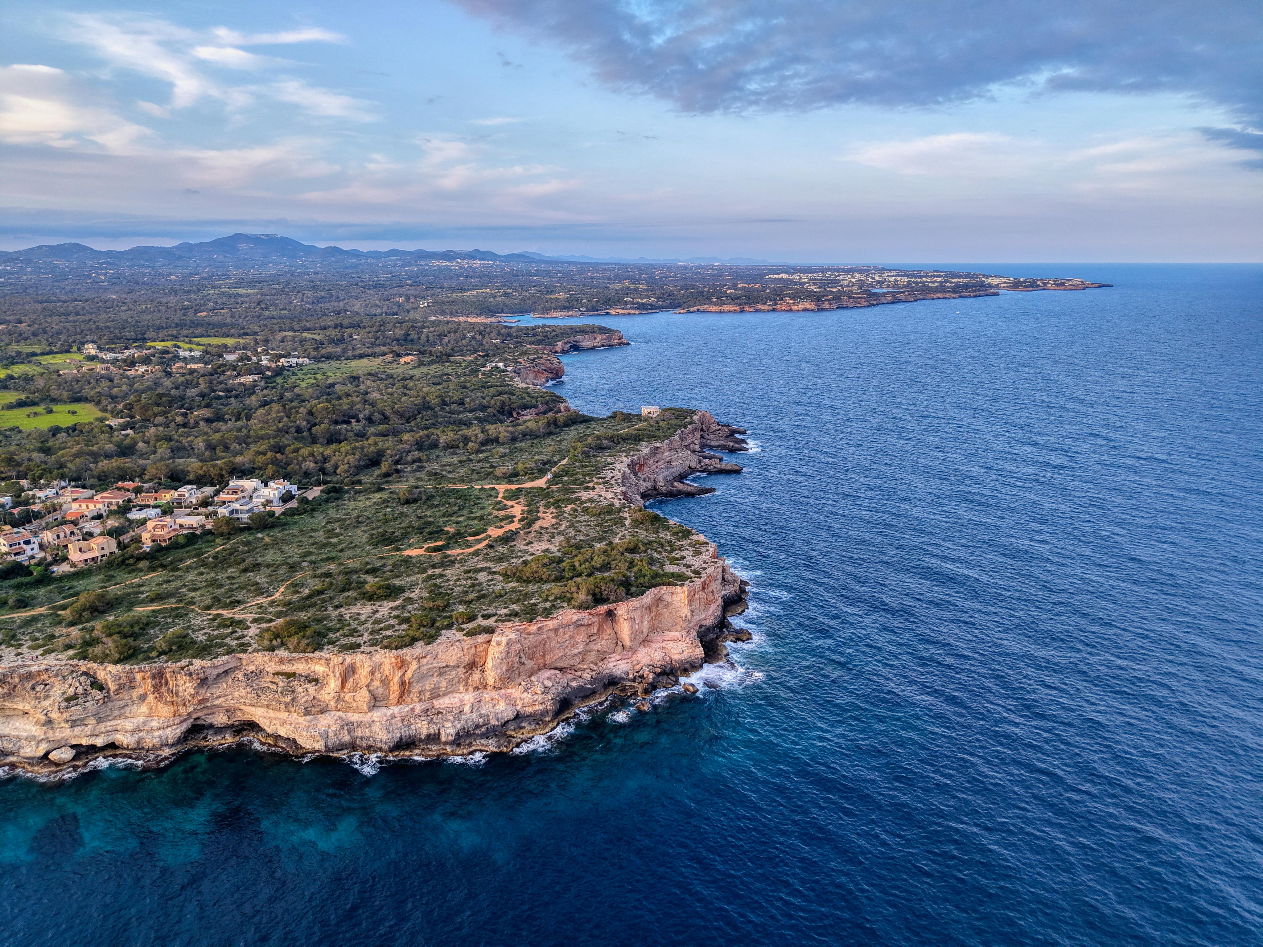 Aerial view of a rocky coastline bordered by blue sea, with countryside stretching inland