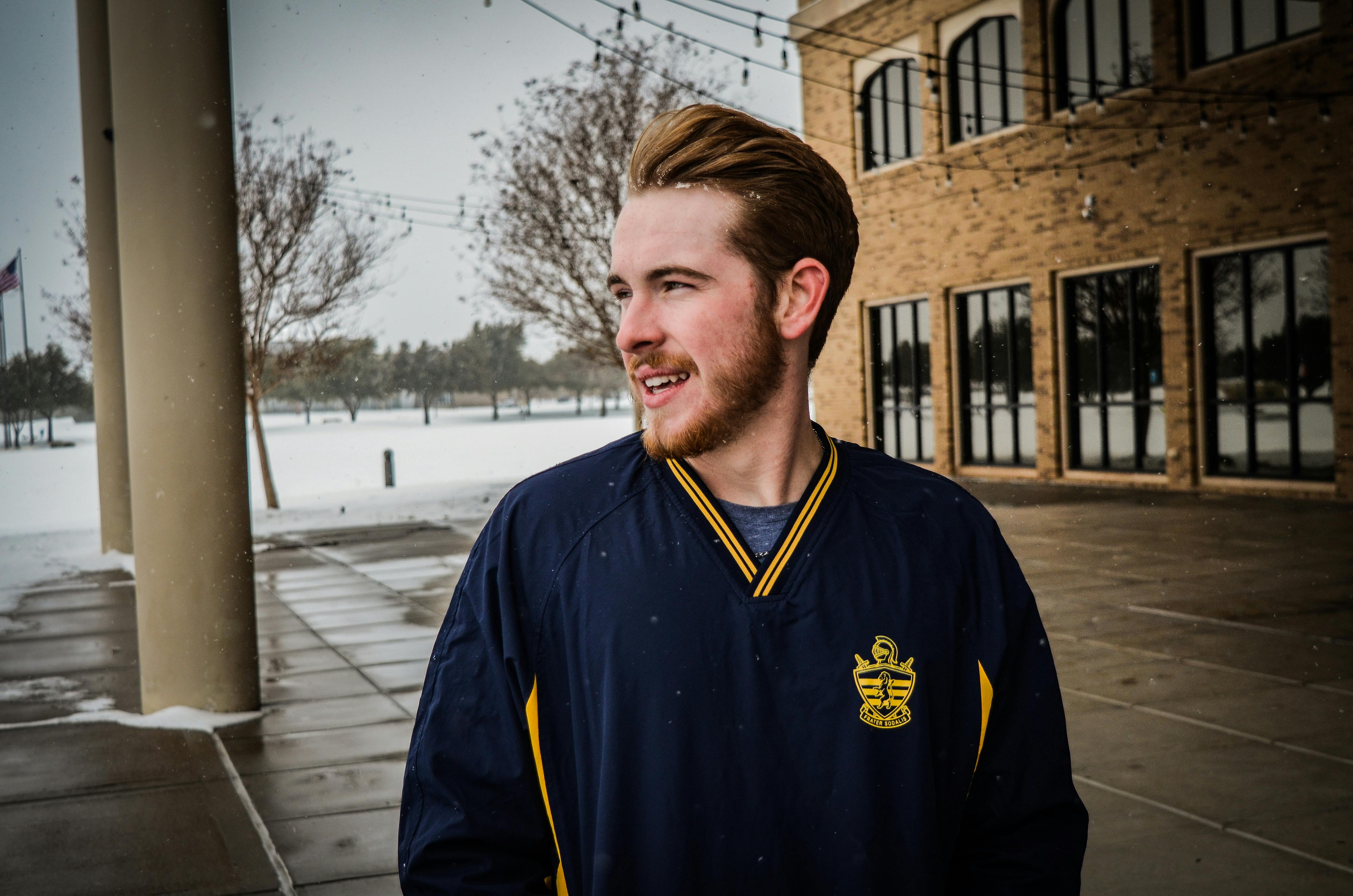 下雪天，一个穿着冬装的年轻人微笑着站在外面的肖像前