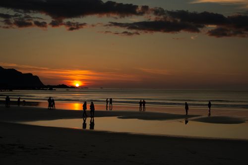 Free Silhouetted people enjoy a calming beach sunset, reflecting a serene and picturesque evening. Stock Photo