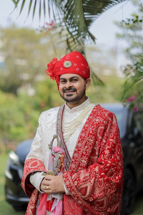 Free Indian groom in lavish red and white traditional clothing posing outdoors, symbolizing cultural richness. Stock Photo