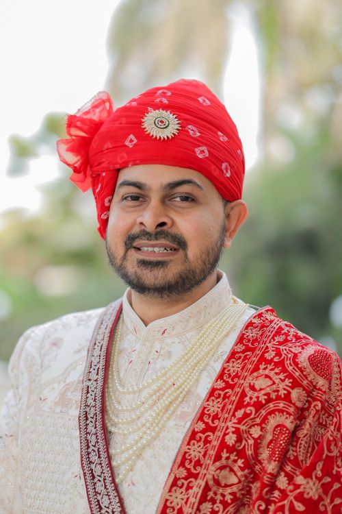 Free Elegant portrait of a traditional Indian groom wearing a red turban and white sherwani outdoors. Stock Photo