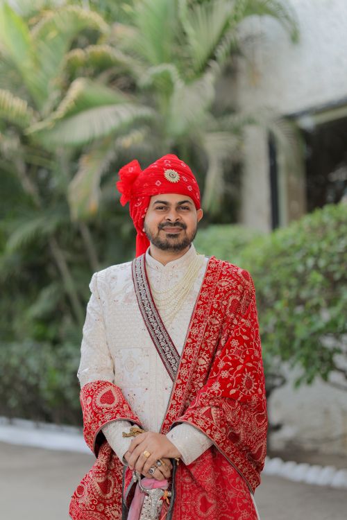 Free A groom in red and white traditional Indian attire, poised and elegant outdoors. Stock Photo