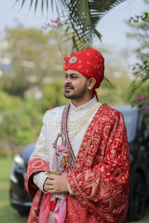 Free A groom in intricate traditional Indian attire poses outdoors with vibrant red and white details. Stock Photo