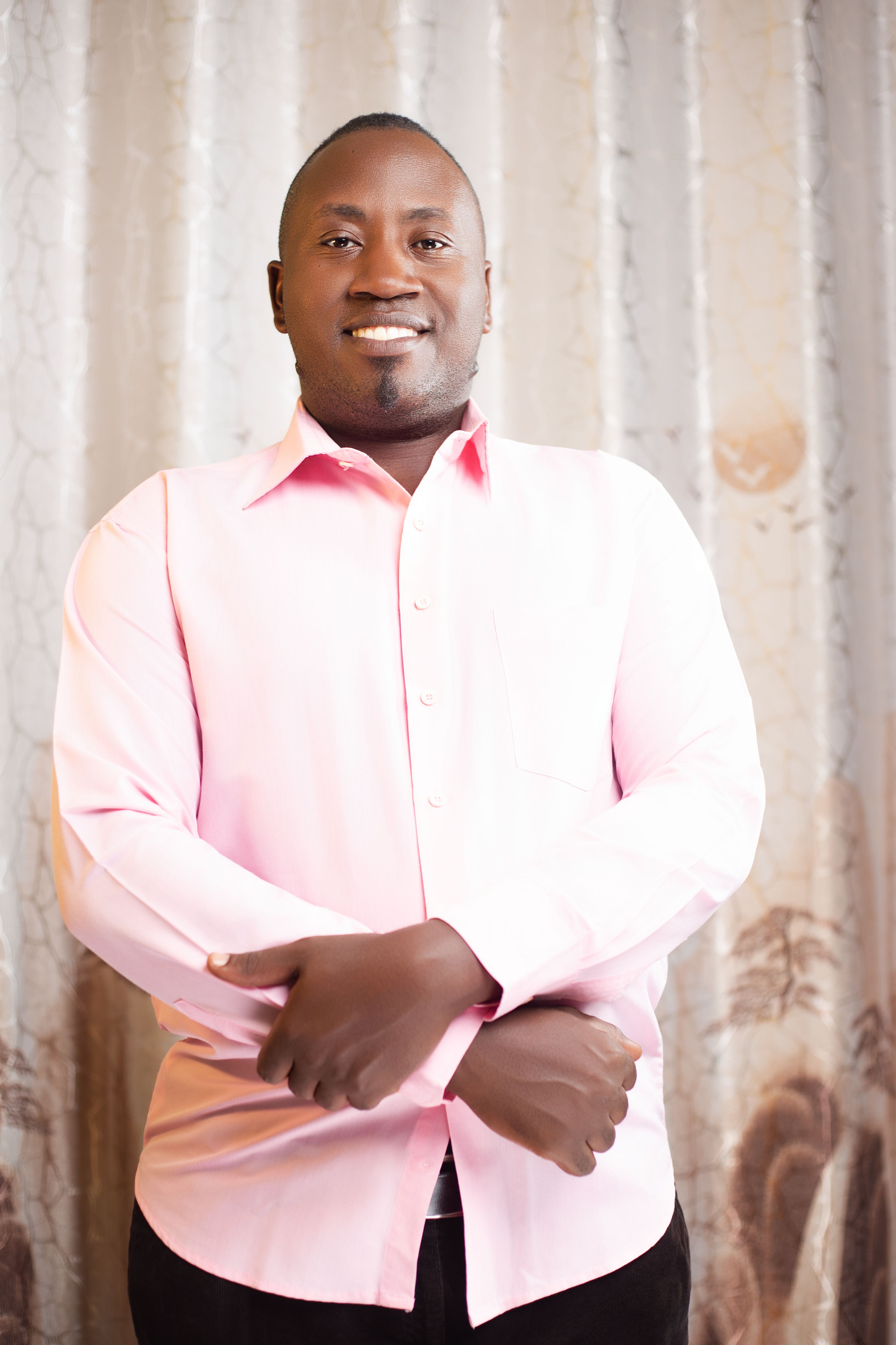 Smiling man in a pink shirt poses confidently indoors against a stylish backdrop.
