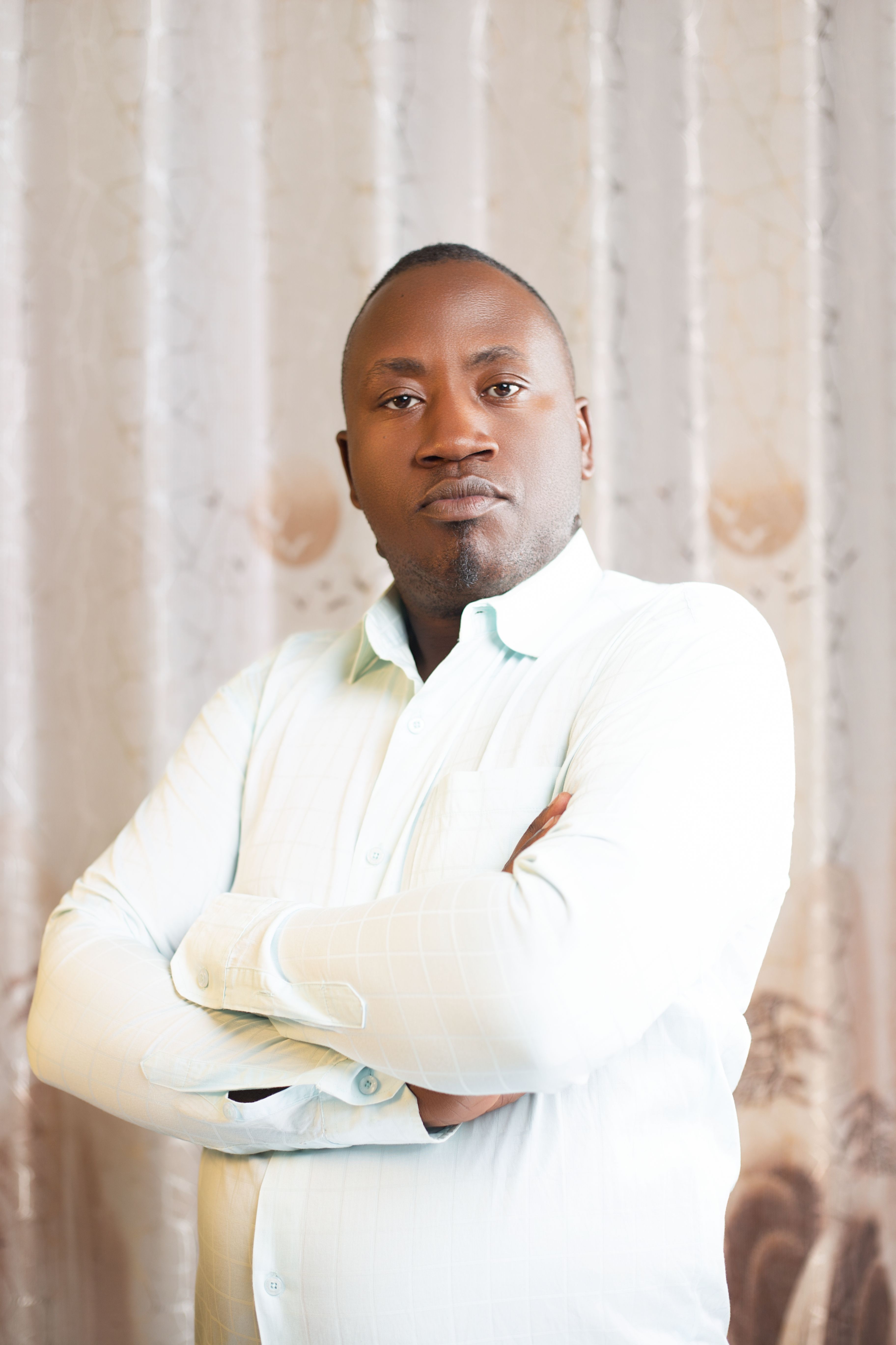Portrait of a confident man wearing a white shirt, posing indoors with folded arms.