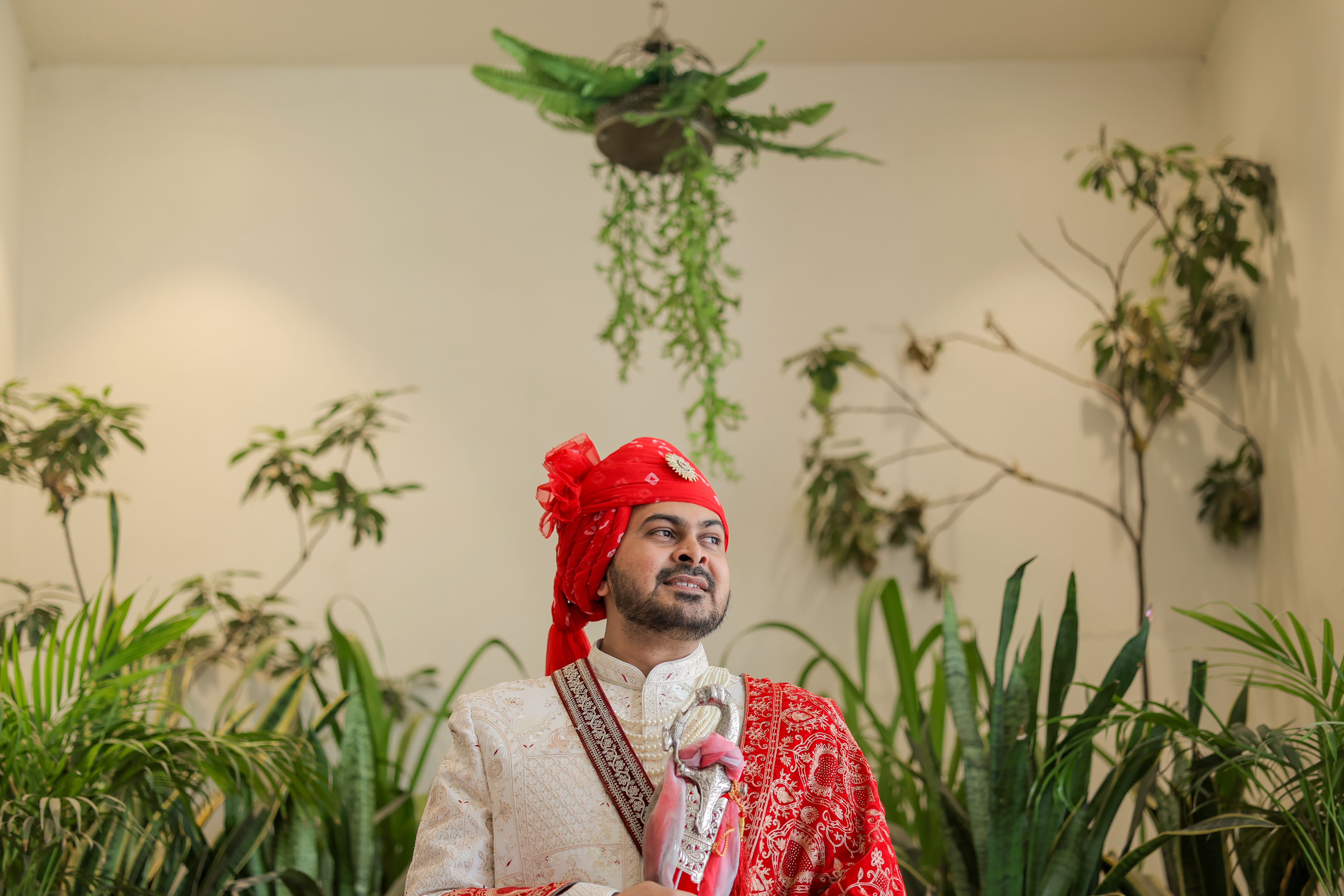 An Indian groom in traditional attire poses amidst indoor greenery, exuding elegance and cultural richness.