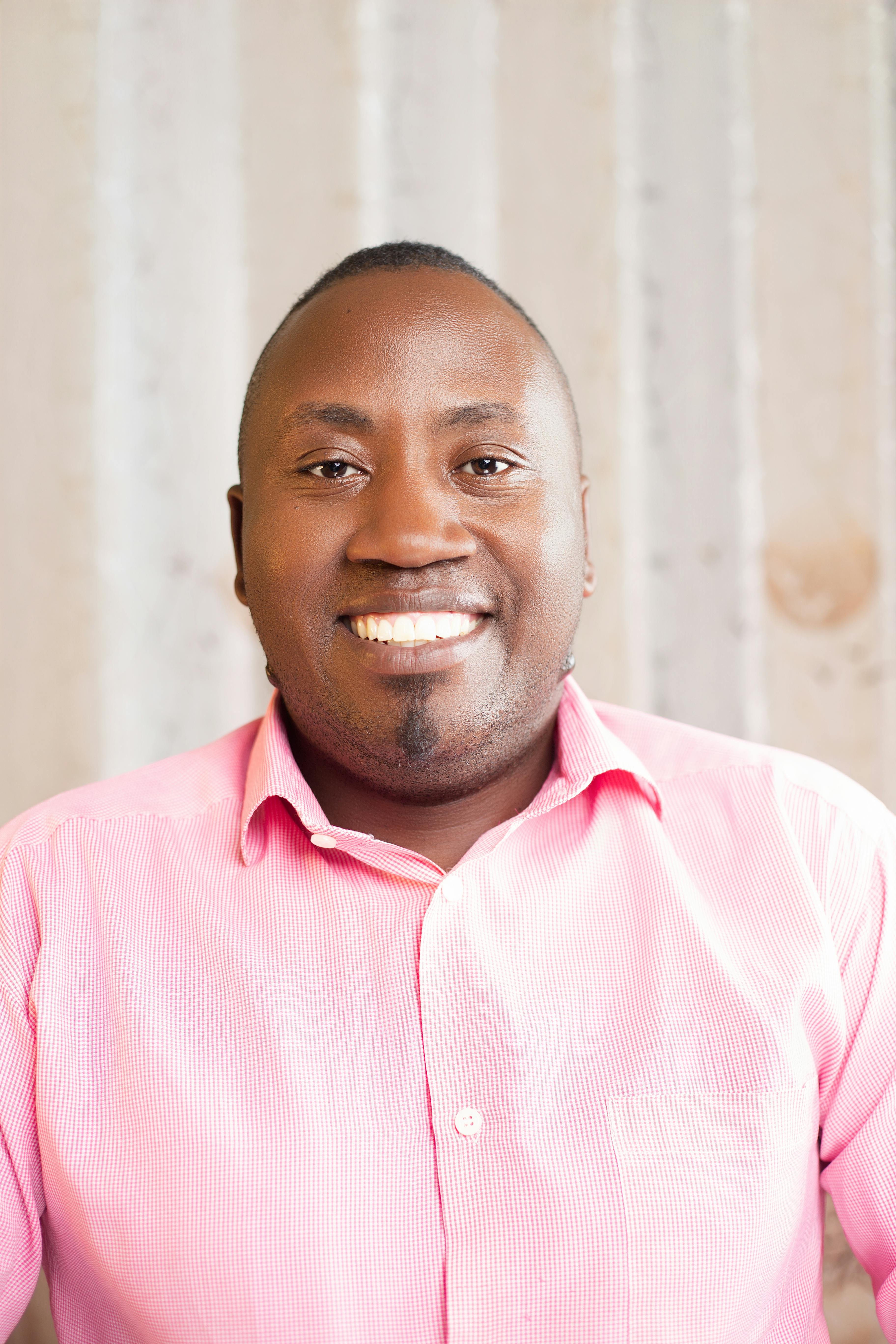 Portrait of a smiling man wearing a pink shirt, photographed indoors.