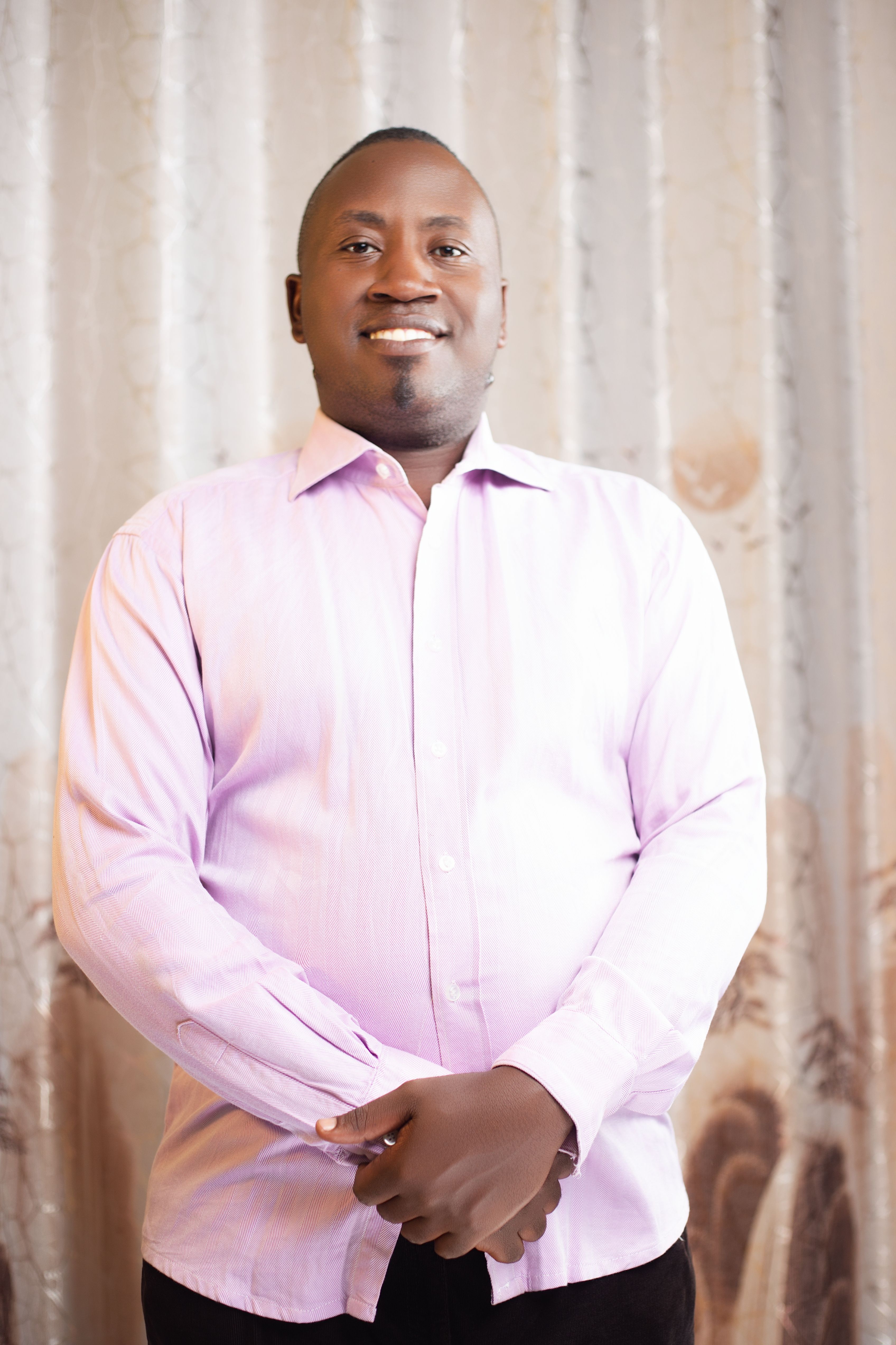 Confident man standing with a smile, wearing a pink shirt, indoors.