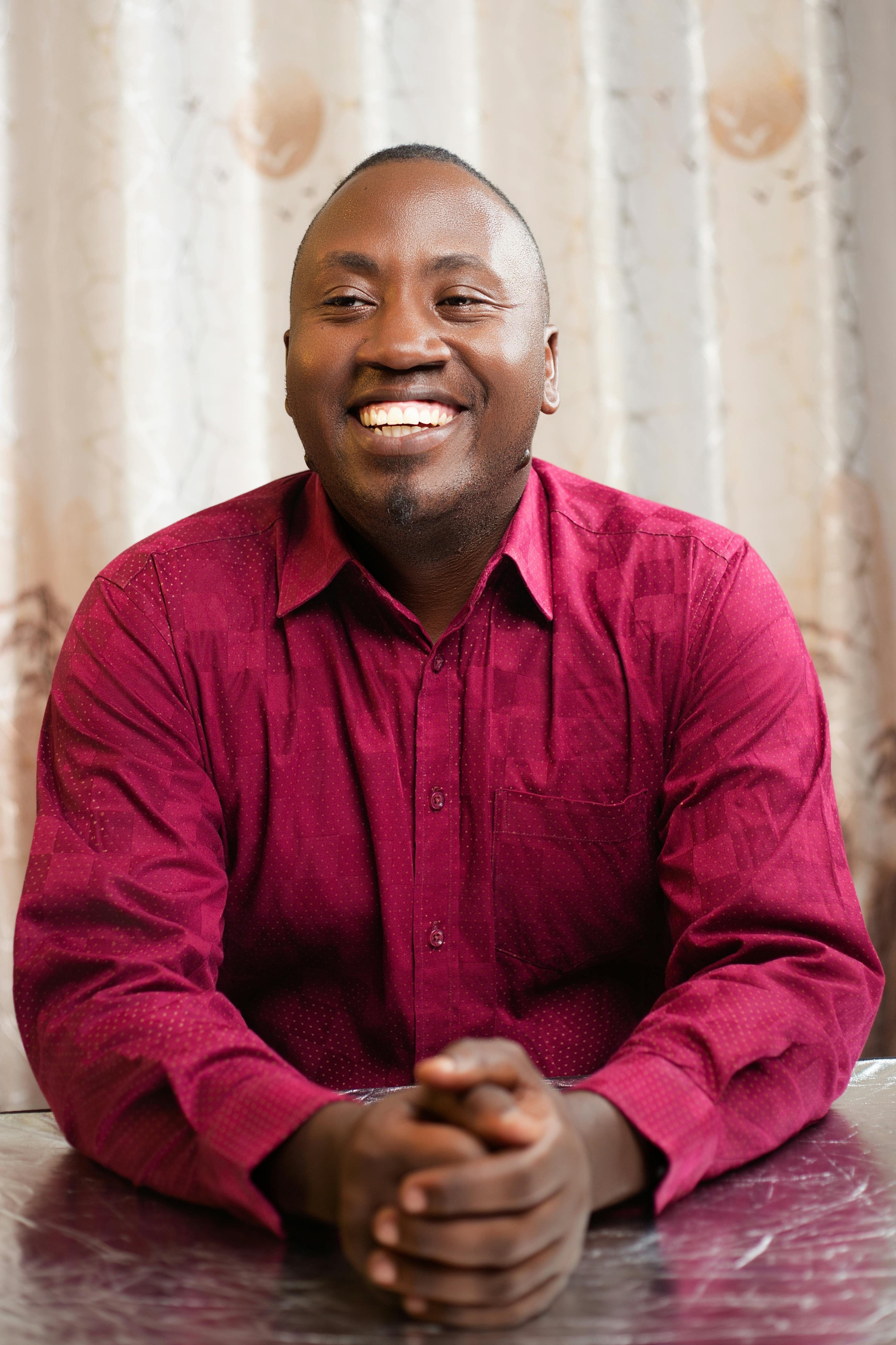 Portrait of a cheerful man in a red shirt sitting indoors, exuding a warm and friendly vibe.