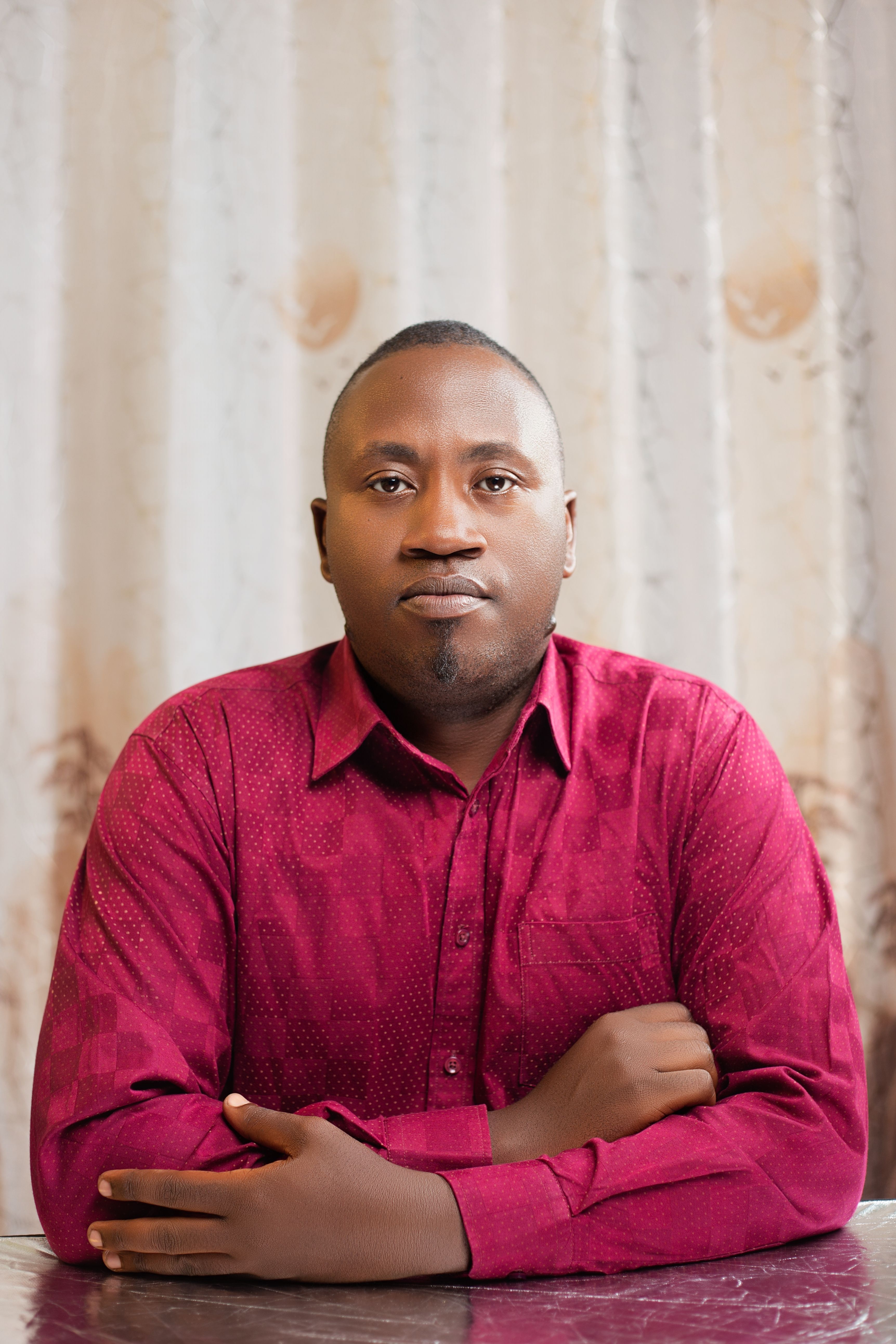 Confident man sitting indoors wearing a red shirt, neutral background.